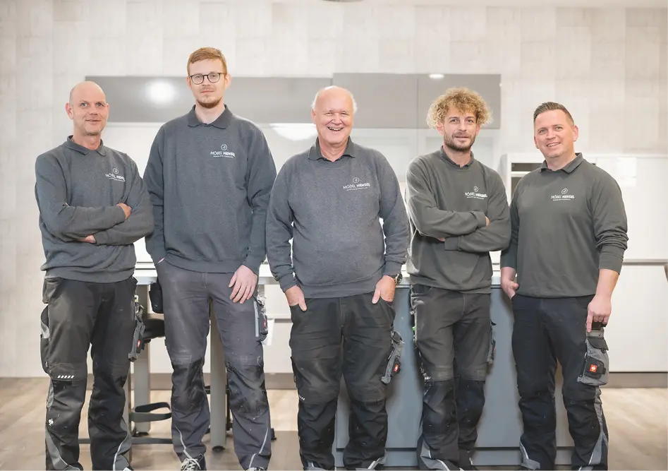 Fünf Männer in Arbeitskleidung mit Logo Möbel Hensel stehen nebeneinander vor einer aufgebauten Küche im Studio